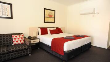A hotel room with a bed, a nightstand, a desk, a chair, and a wall-mounted air conditioner.