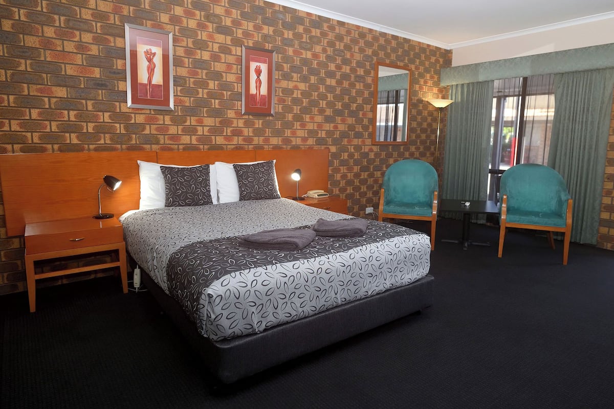 Hotellihuone, jossa on tiilikuviollinen seinä, suuri sänky kuviollisilla vuodevaatteilla, kaksi yöpöytää valaisimineen, työpöytä tuolilla ja peili seinällä.