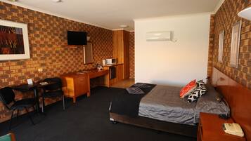 Habitación de hotel con pared de ladrillo, cama con cubrecama gris y negro, escritorio de madera con silla, televisor montado en la pared y mesita de noche con lámpara y teléfono.