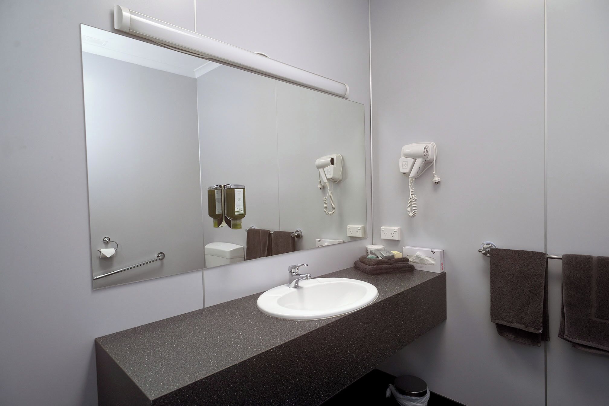 A modern bathroom with a large mirror, a white sink, a hairdryer, and a towel rack.
