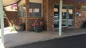 A building with a brick facade, large windows, and a reception area. There are potted plants with pink flowers in front. - Horsham Mid City Court Motel (Horsham)