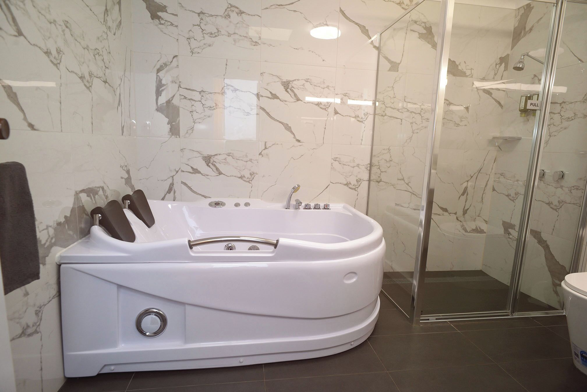 A modern bathroom with a large white bathtub, a glass-enclosed shower, and marble walls.