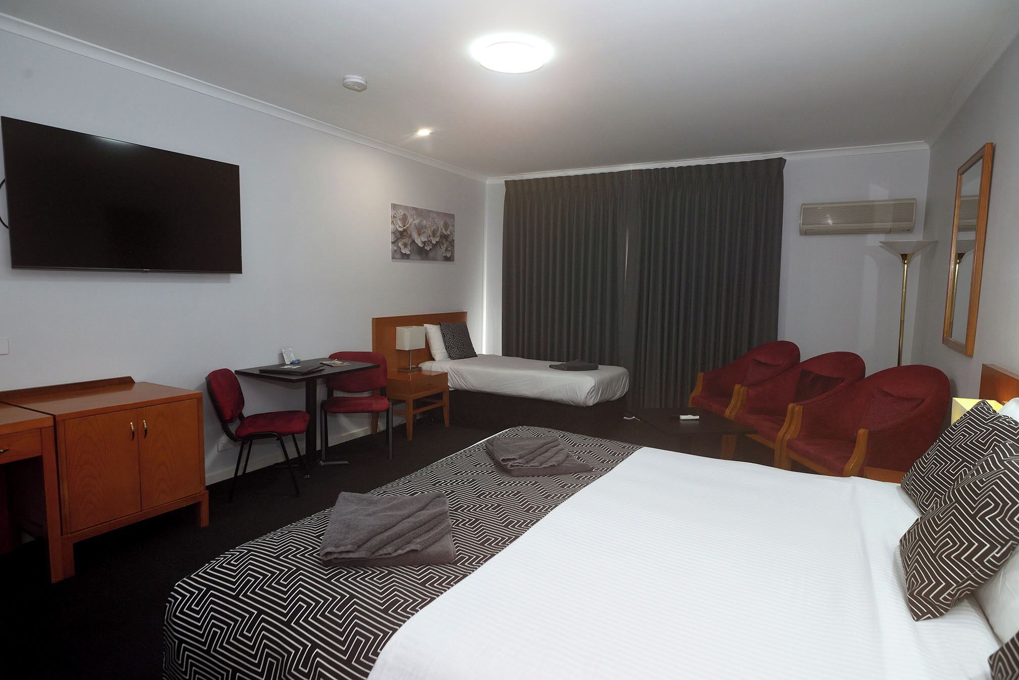 A hotel room with a bed, a desk, a chair, a TV, and a window with curtains.