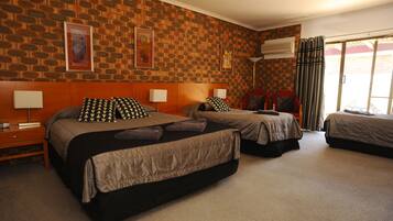 Habitación de hotel con tres camas, pared de ladrillo y un ventanal con cortinas.