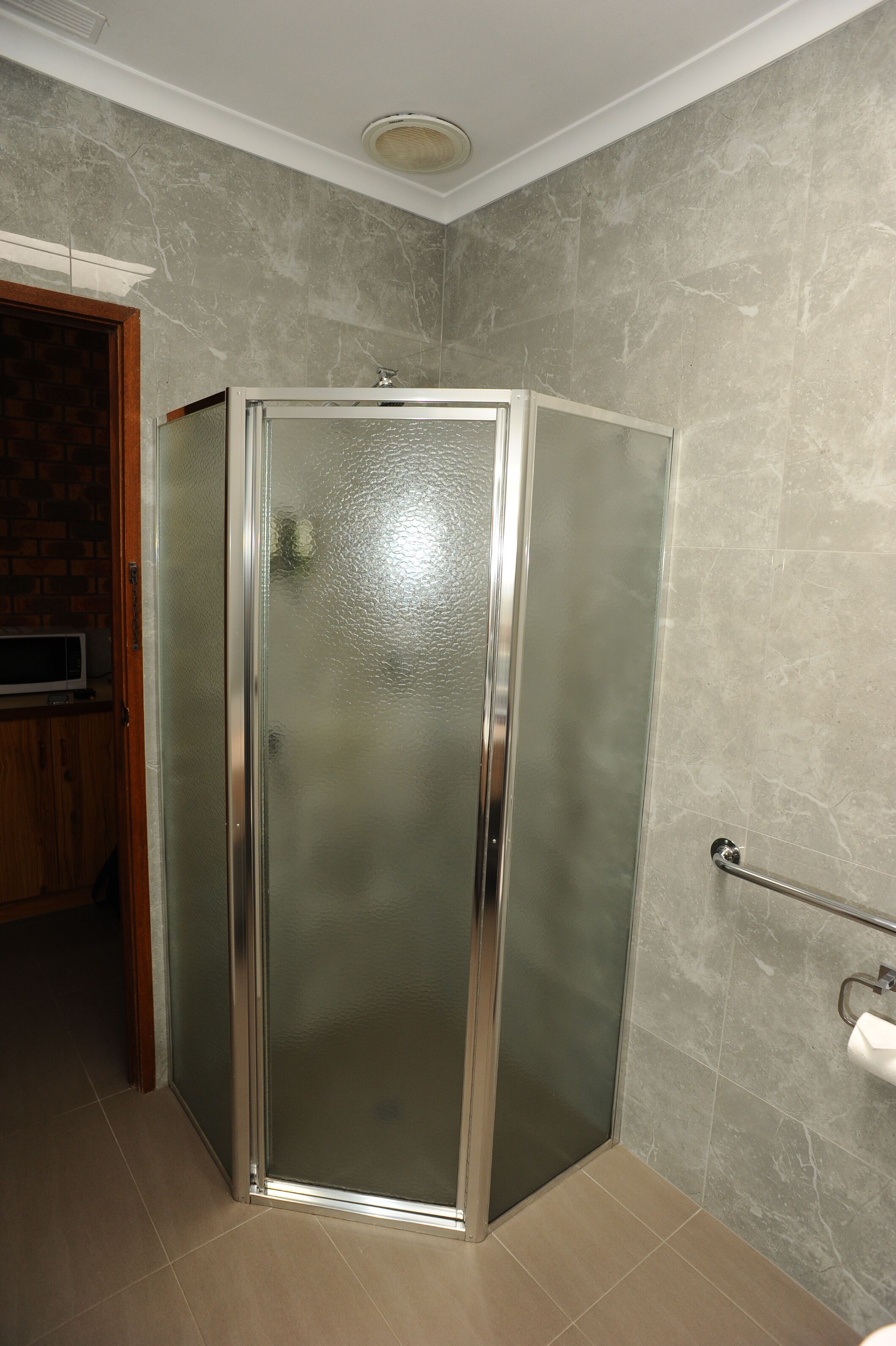 Un baño con cabina de ducha de vidrio, barra de apoyo y soporte para papel higiénico en la pared.