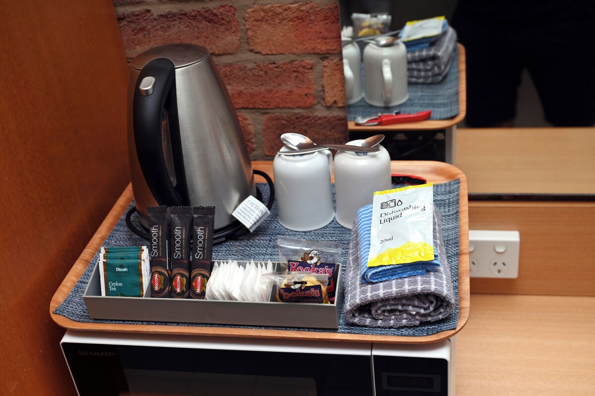 Tarjotin, jossa on kahvinkeitin, teepusseja, pullo astianpesuainetta ja pientä purtavaa.