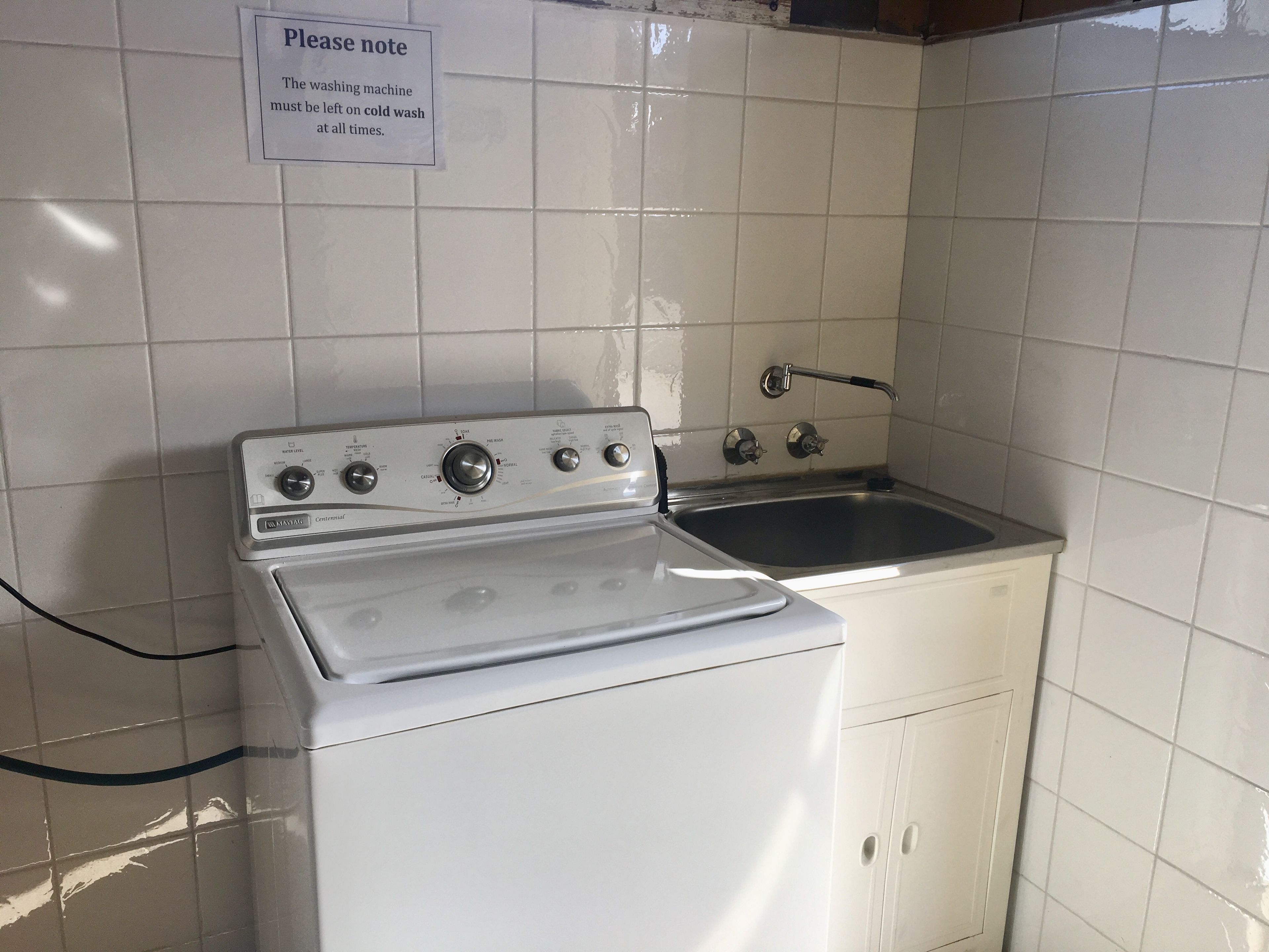 A kitchen with a stove, sink, and a sign instructing to leave the washing machine on cold wash.