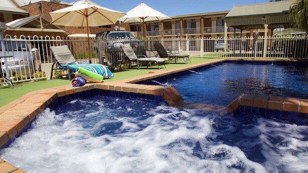 Une piscine avec un jacuzzi, entourée de chaises longues et de parasols.
