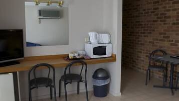 A kitchenette with a microwave, a small fridge, and a TV. There are two chairs and a table with a trash bin.