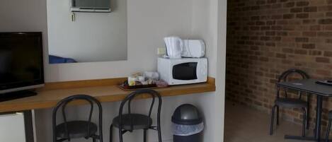 A kitchenette with a microwave, a small fridge, and a TV. There are two chairs and a table with a trash bin.