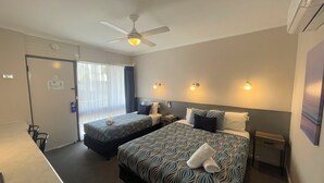 Une chambre d’hôtel avec deux lits, un ventilateur de plafond, un bureau et une fenêtre avec des rideaux.