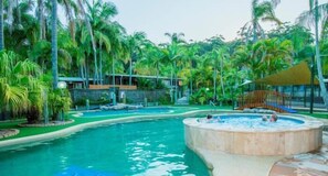 A swimming pool surrounded by palm trees and a hot tub area. - The Palms At Avoca (Avoca Beach)