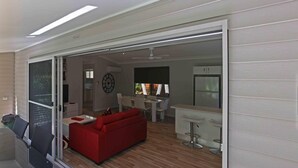 Una sala de estar moderna con un sofá rojo, una zona de comedor con sillas blancas y una cocina con refrigerador.