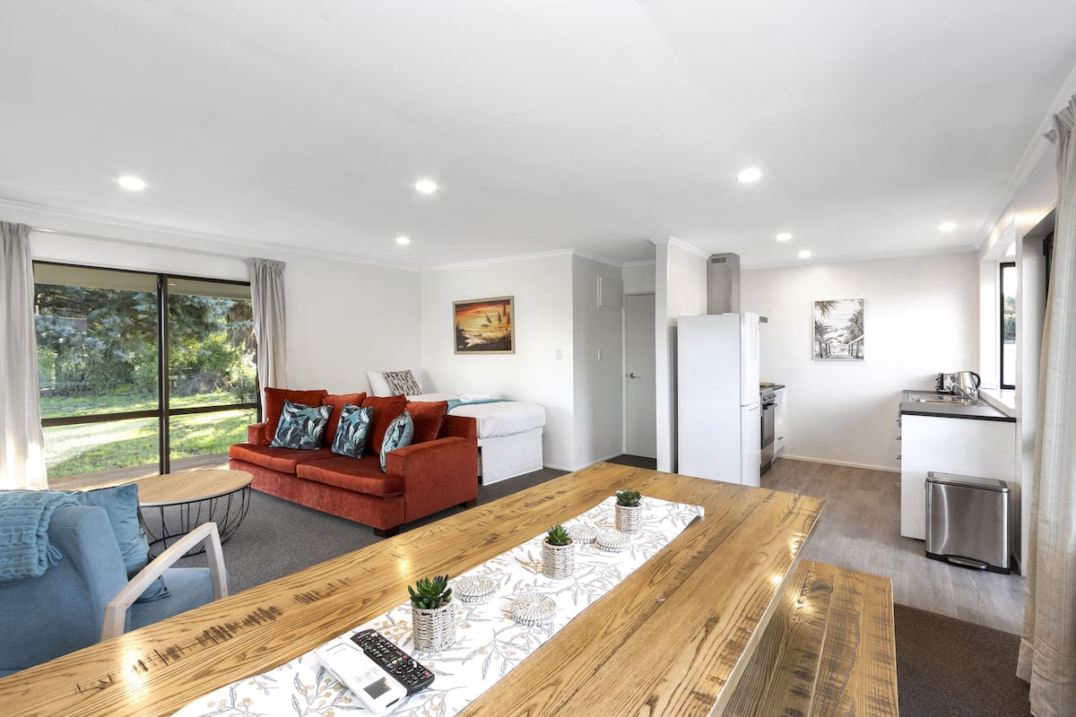 Ein modernes Wohnzimmer mit einem roten Sofa, einem Holzesstisch und einer Küchenzeile inklusive Kühlschrank und Spüle.