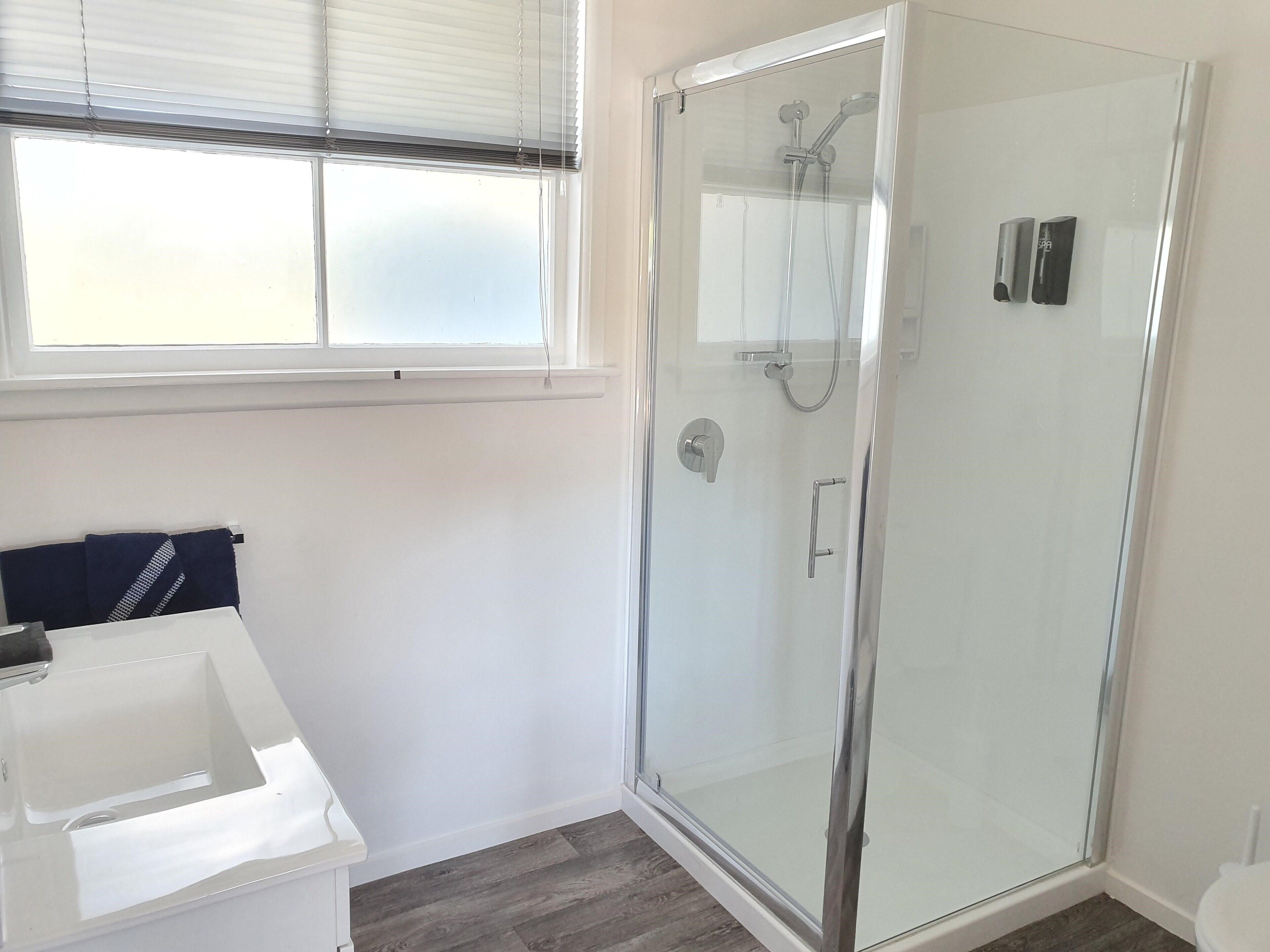 Une salle de bain moderne avec une douche à parois de verre, un lavabo blanc et une fenêtre équipée de stores.