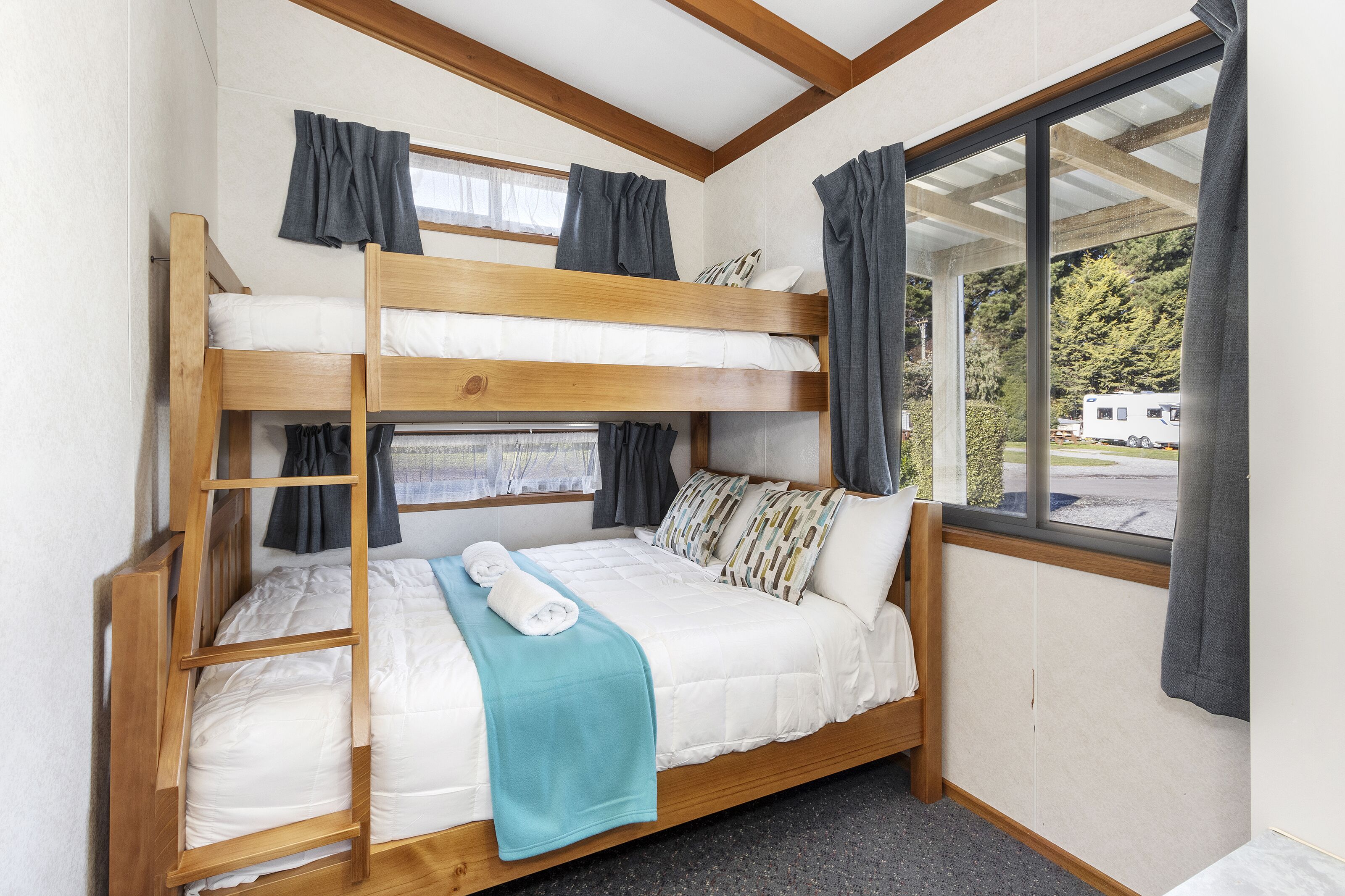 A bunk bed room with a window view, curtains, and a ladder.