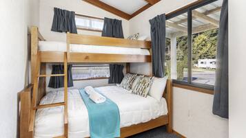 A bunk bed room with a window view, curtains, and a ladder.