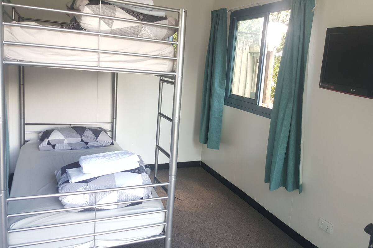 Une chambre avec des lits superposés, un téléviseur fixé au mur et des rideaux.