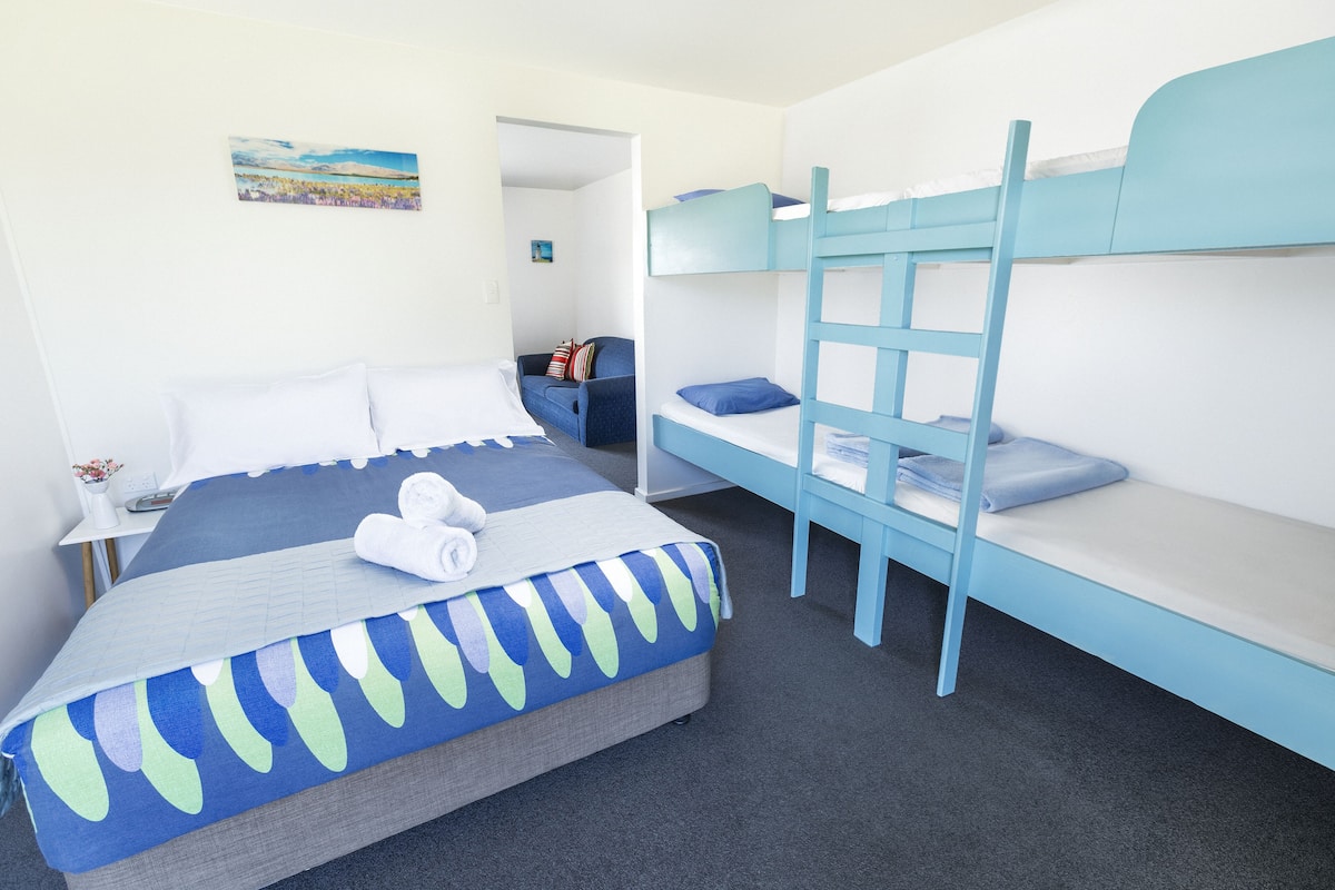 Une chambre avec un lit superposé, un lit simple et un bureau avec une chaise.