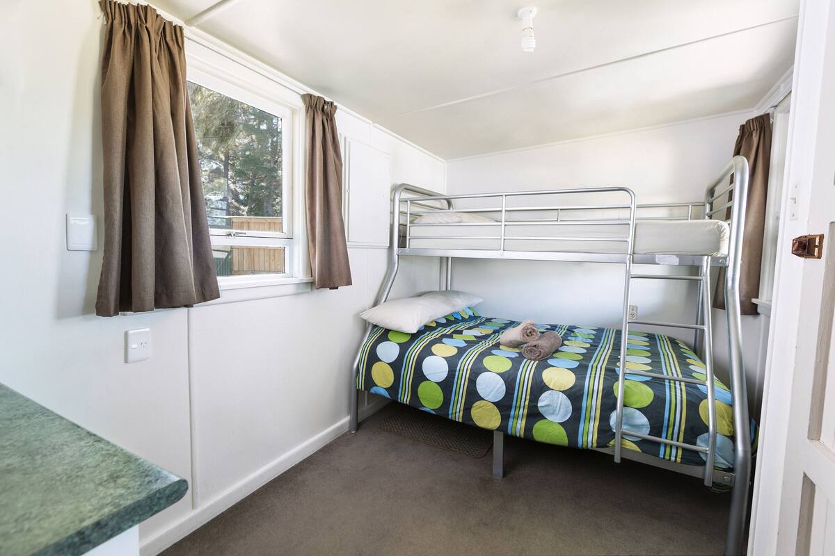 Un lit superposé avec une couvre-lit à pois, une fenêtre avec des rideaux et un petit coin cuisine.