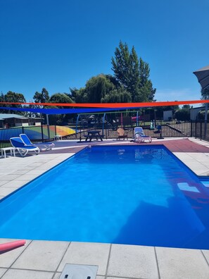 Una piscina con agua azul, rodeada por un solárium con baldosas y sillas de descanso.