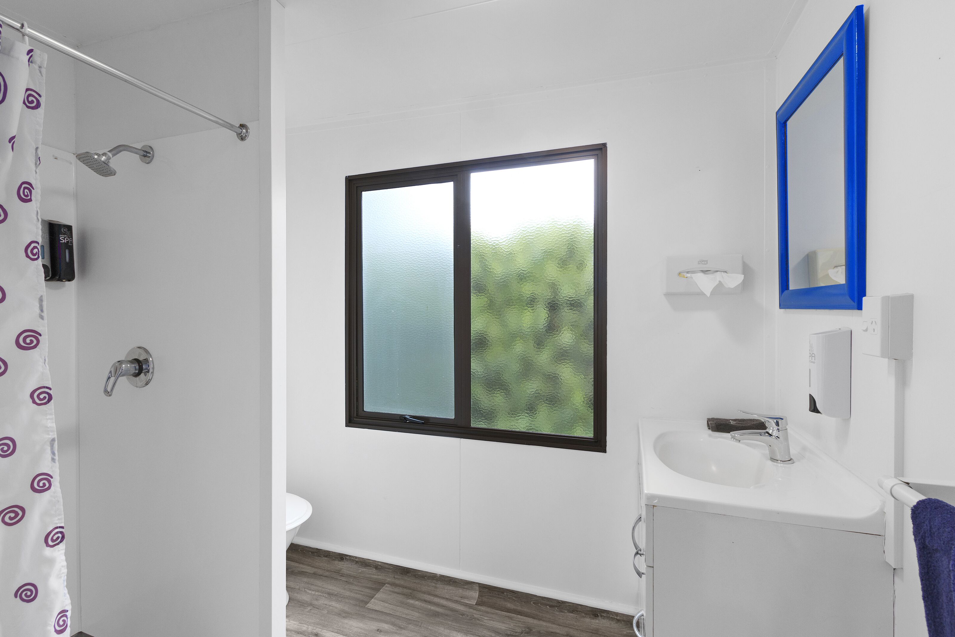 A bathroom with a shower, a window, a sink, and a mirror.