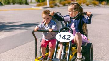 Deux enfants sont à bord d’un petit véhicule jaune, portant un numéro d’identification, et circulent sur une route asphaltée.