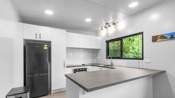 Een moderne keuken met witte kasten, een roestvrijstalen koelkast, een ingebouwde oven en een raam met uitzicht op groen.
