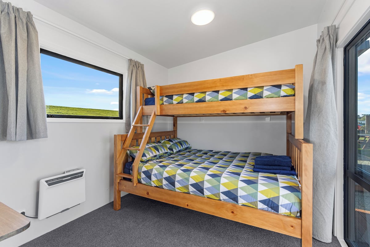 Ein Stockbett mit einer Leiter, ein Fenster mit Blick auf ein grünes Feld und eine weiße Heizung.