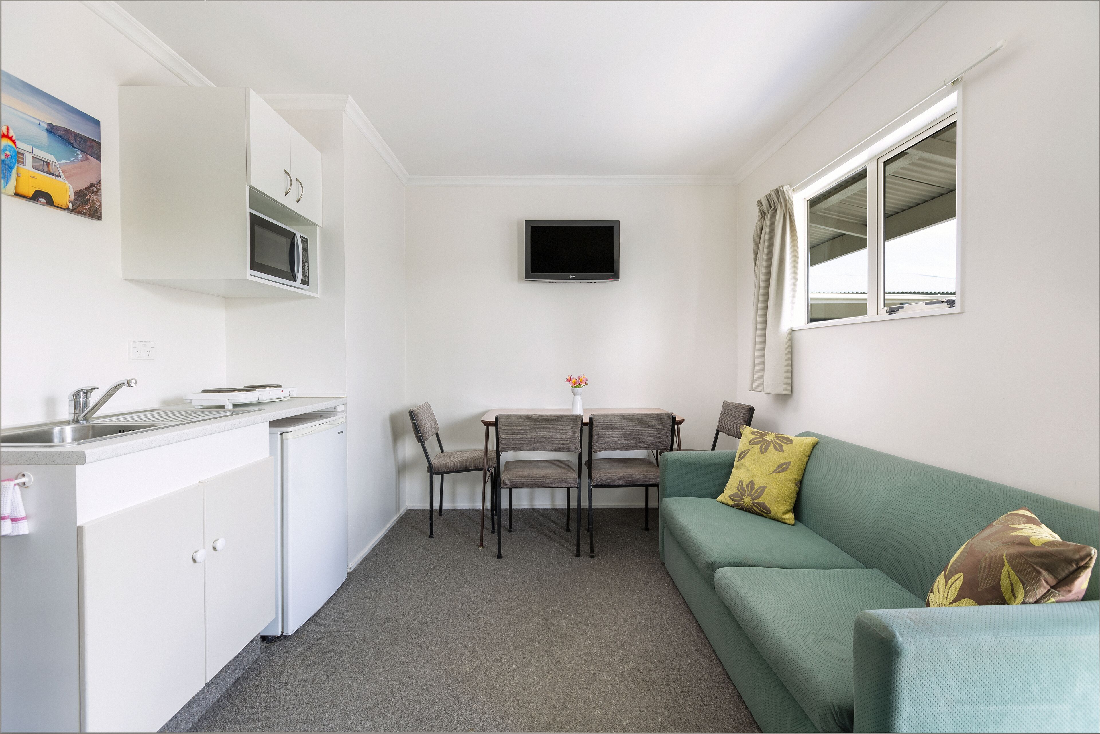 A compact kitchen with a microwave, a sink, and a dining area with chairs and a table.