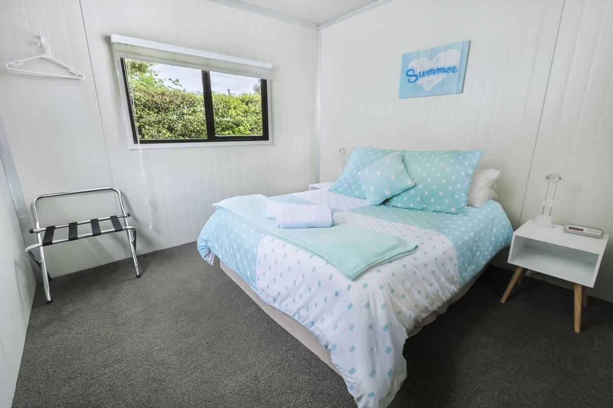 Une chambre à coucher comprenant un lit, une table de chevet, une commode, une fenêtre, une lampe suspendue et un tableau accroché au mur.