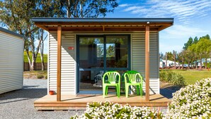 Een klein, gelijkvloers gebouw met een houten veranda, twee groene plastic stoelen en een deur met een rood bord.