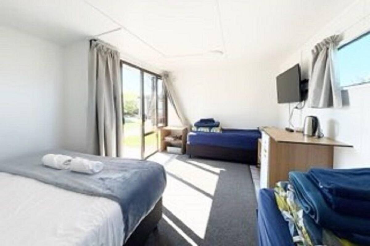 Ein Hotelzimmer mit einem Bett, einem Schreibtisch mit Stuhl, einem Fernseher und einem Fenster mit Vorhängen.