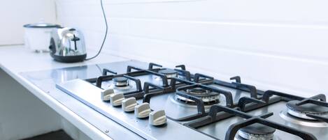 A kitchen with a gas stove, a kettle, and a white countertop.