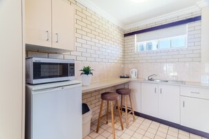Una cocina con armarios blancos, un microondas, taburetes y un ventanal.