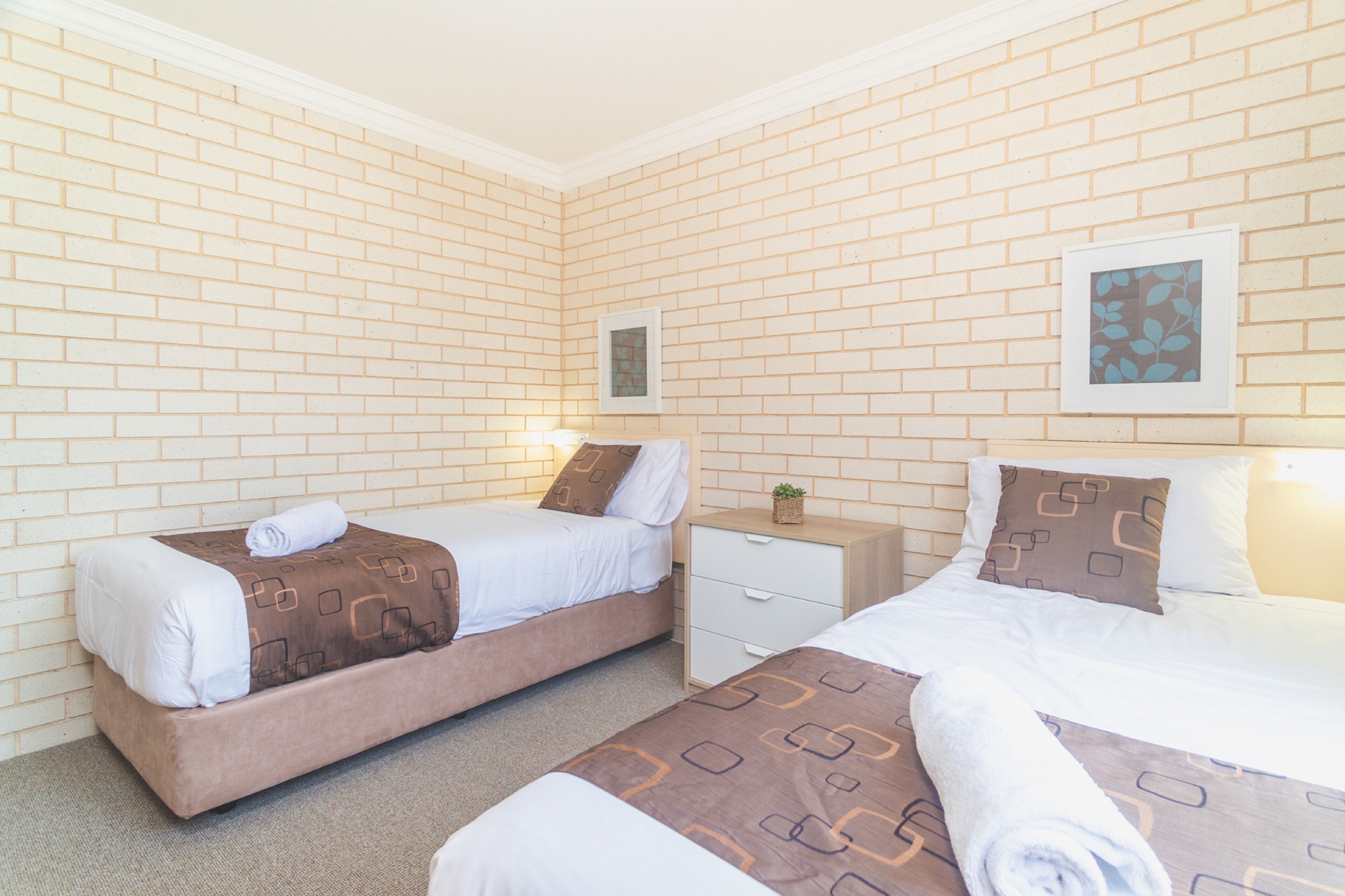 A hotel room with two beds, a small bedside table, a nightstand, and a framed picture on the wall.