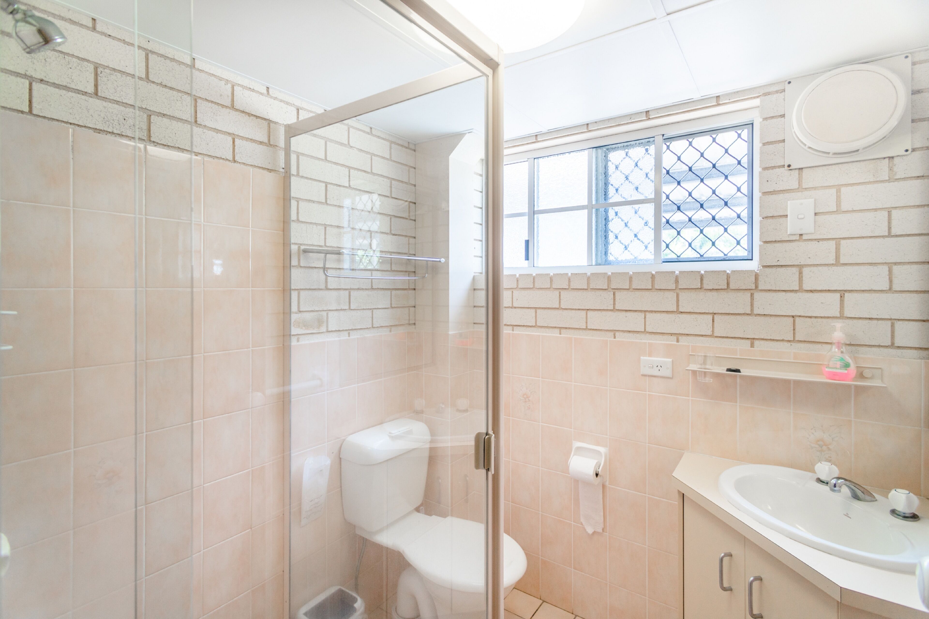 Un baño con ducha envuelta en vidrio, inodoro, lavamanos y ventana con vistas.
