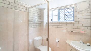 Un baño con ducha envuelta en vidrio, inodoro, lavamanos y ventana con vistas.