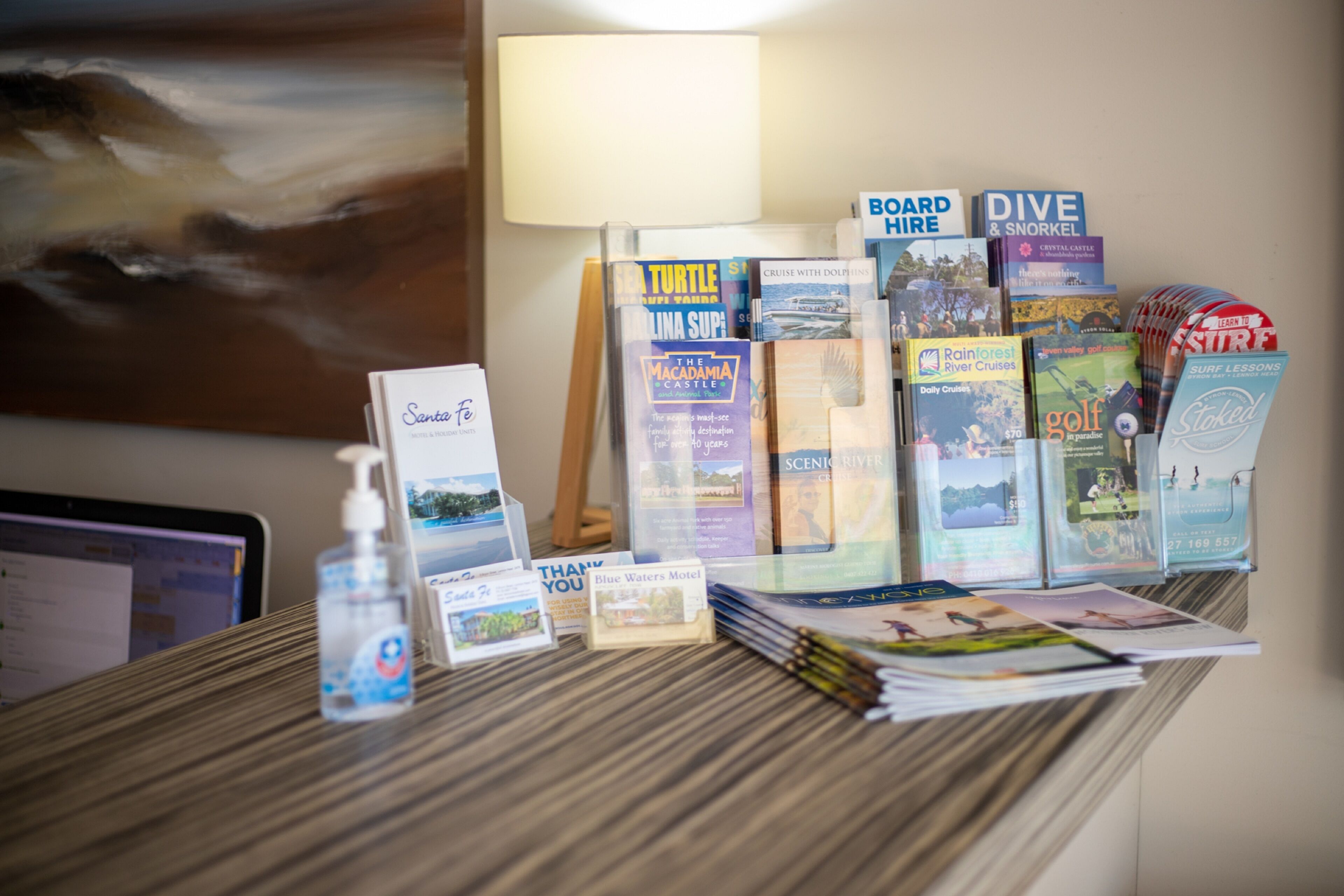A desk with travel brochures, a bottle of hand sanitizer, and a thank you card.