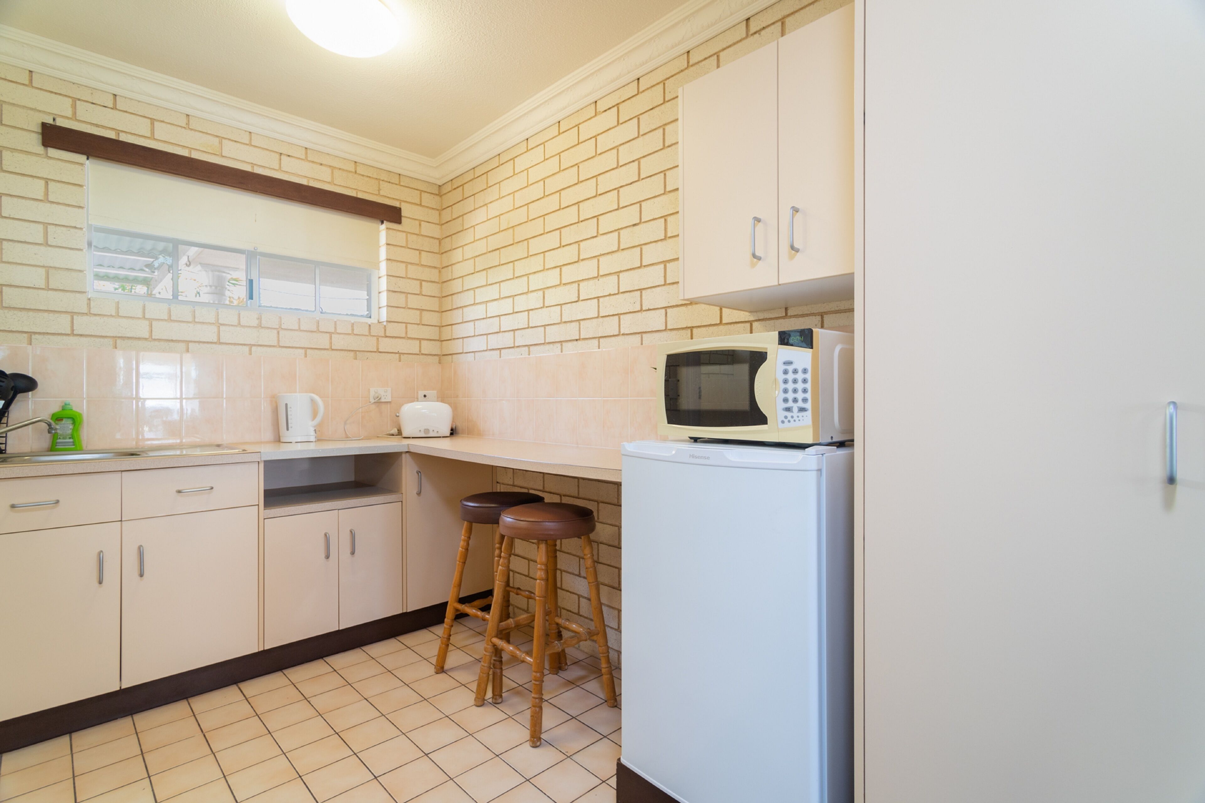 A kitchen with white cabinets, a microwave, a refrigerator, and two stools.