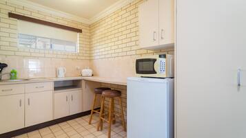 A kitchen with white cabinets, a microwave, a refrigerator, and two stools.