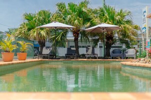 Una piscina al aire libre, sombrillas, sillones reclinables de piscina