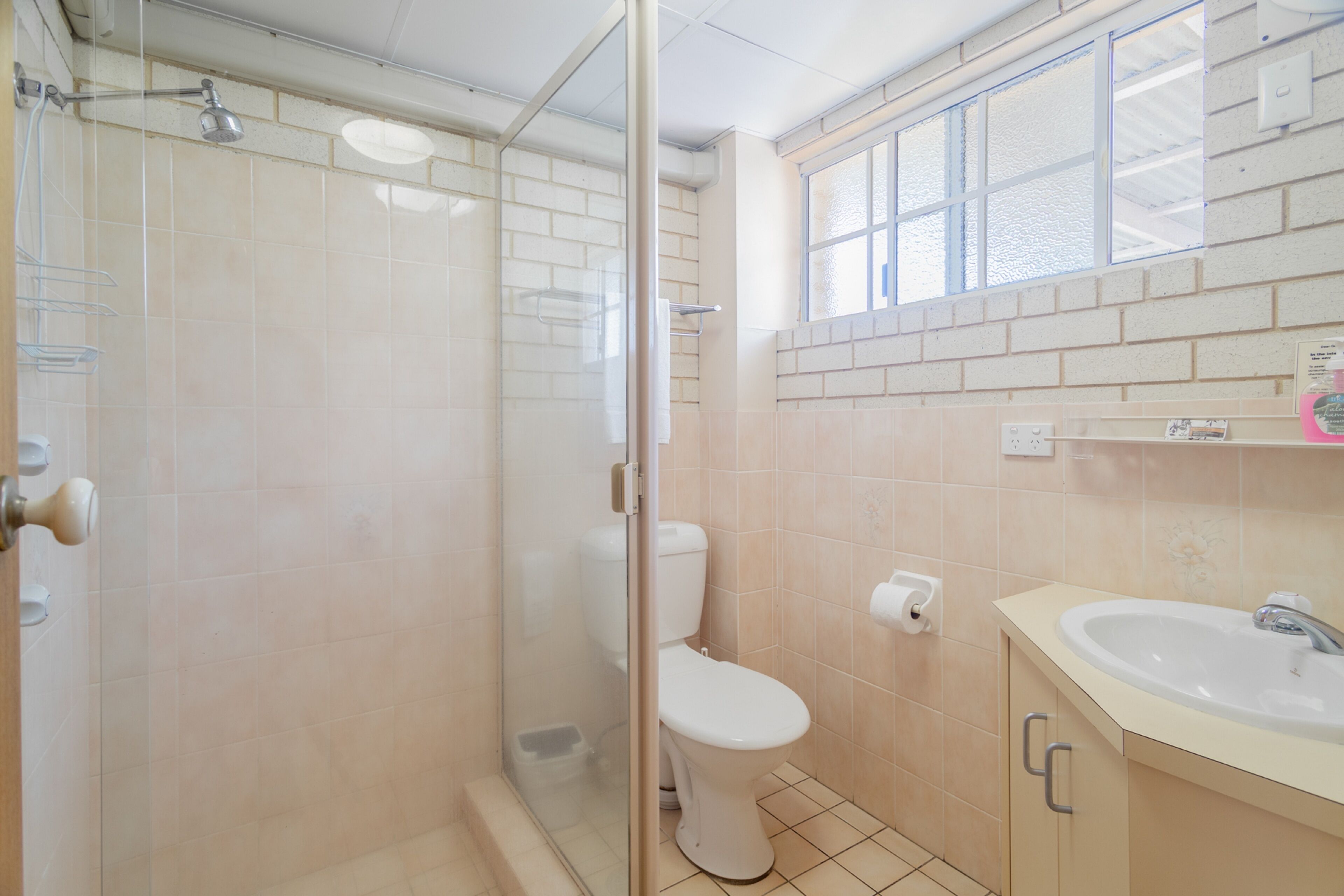 A bathroom with a glass-enclosed shower, a toilet, and a sink with a mirror above it.