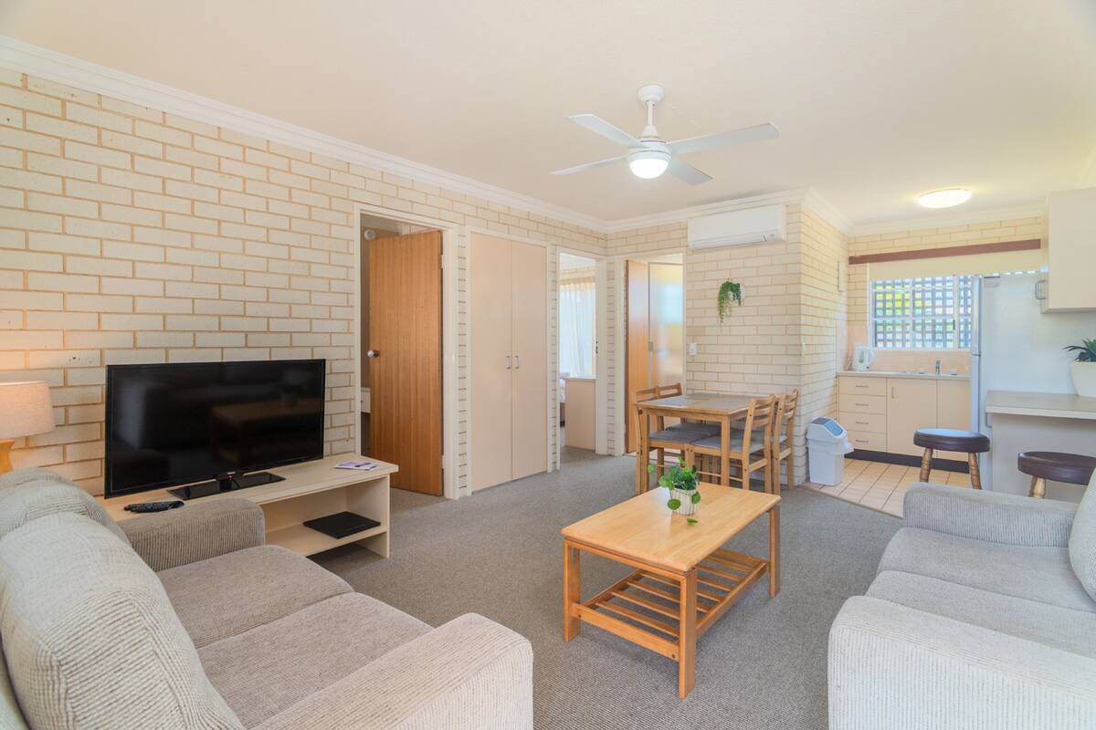A living room with a TV, sofas, a wooden table, and a ceiling fan.
