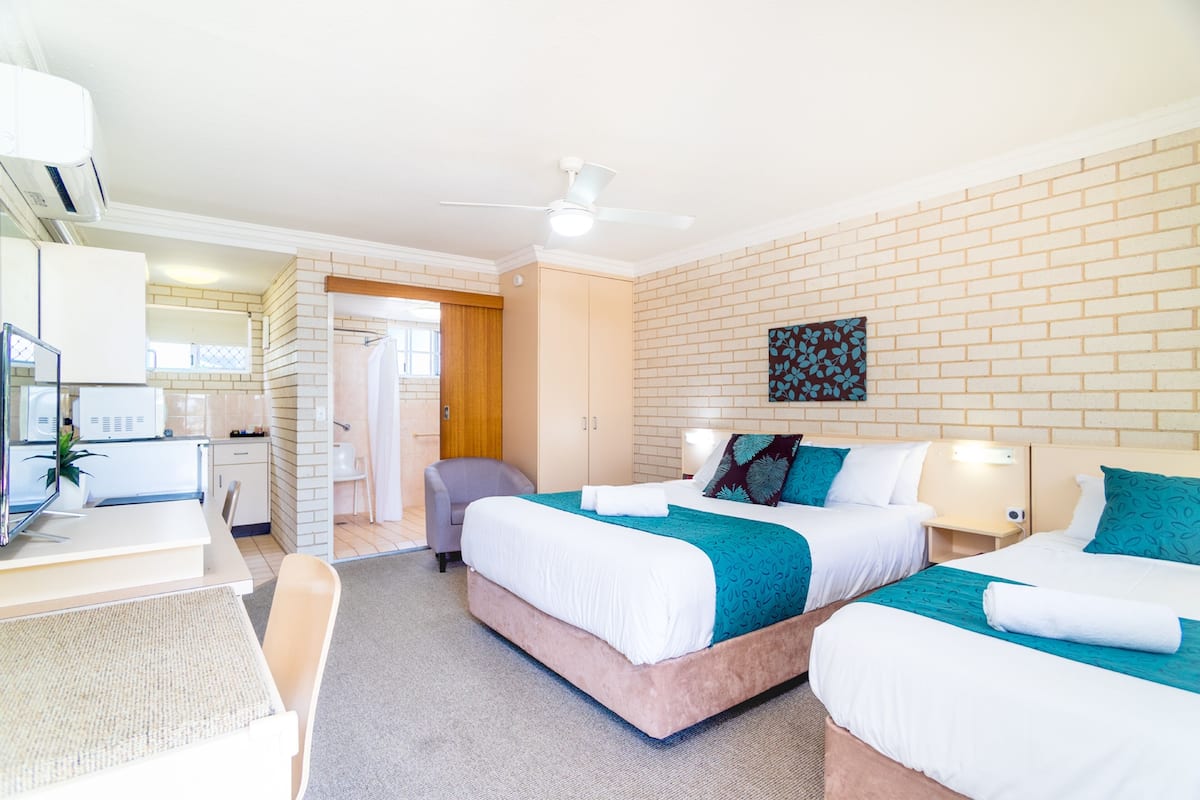 A hotel room with two beds, a desk, a chair, a TV, and a ceiling fan.