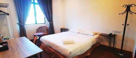 A hotel room with a bed, a desk, a chair, a coat rack, and a window with curtains.