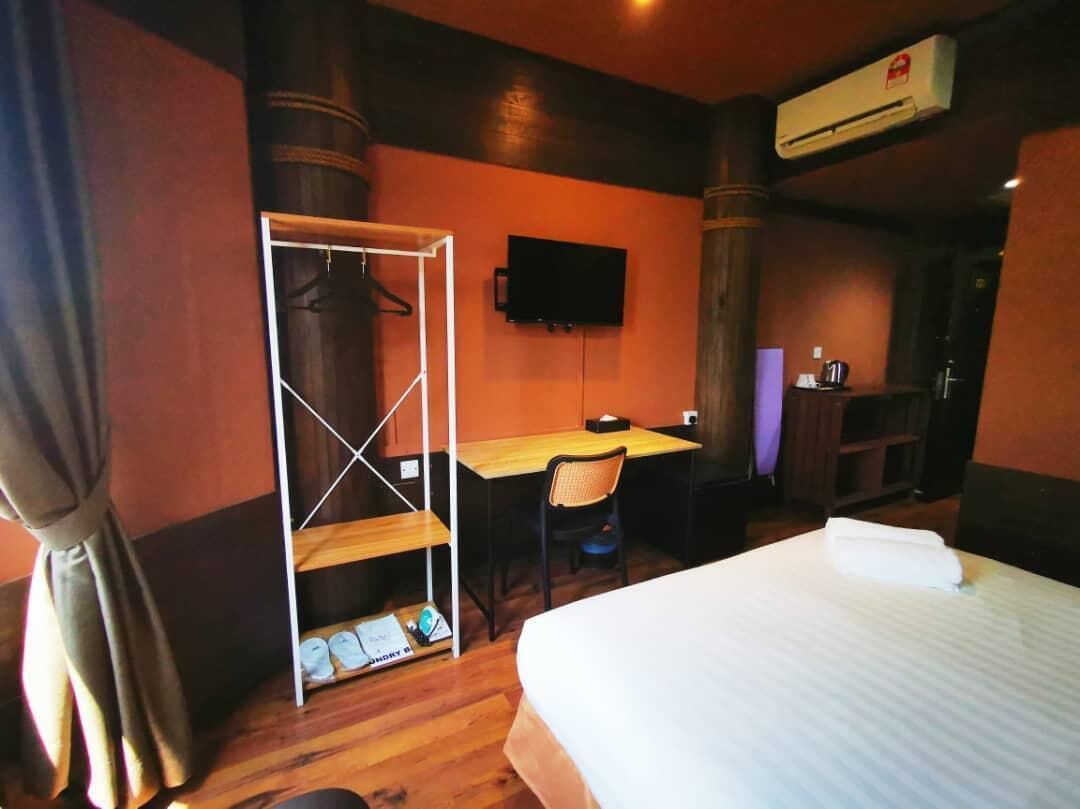 Quarto de hotel com cama, escrivaninha, cadeira, guarda-roupa e televisão.