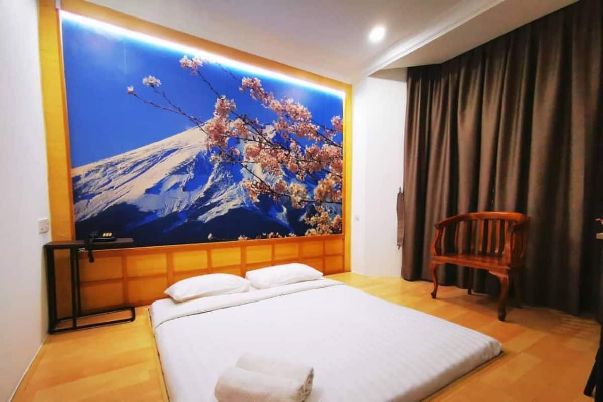 A hotel room with a large bed, a wooden chair, and a wall mural of a mountain and cherry blossoms.
