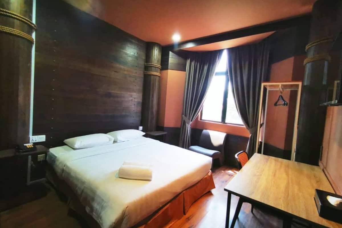 A hotel room with a large bed, a wooden table, and a window with curtains.