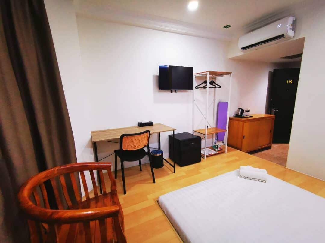 A hotel room with a bed, a desk, a chair, a TV, a wardrobe, and a door with the number 119.